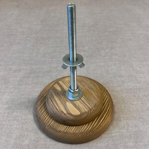 May include: A wooden base with a metal screw and a wing nut. The base is made of two layers of wood with a grain pattern.