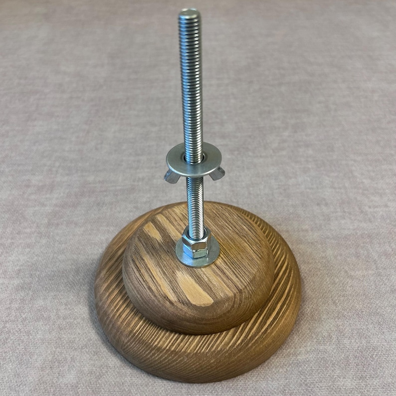 May include: A wooden base with a metal screw and a wing nut. The base is made of two layers of wood with a grain pattern.