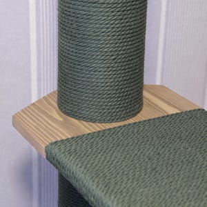 May include: Close-up of a green sisal-covered cat scratching post with a wooden platform. The post is wrapped in thick, tightly woven sisal rope.