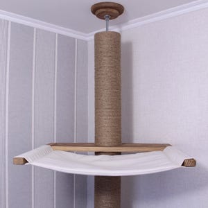 May include: A ceiling-mounted cat tree with a sisal-wrapped post and a wooden platform supporting a white hammock. The top features a wooden cap. The cat tree is designed to be installed in a corner.