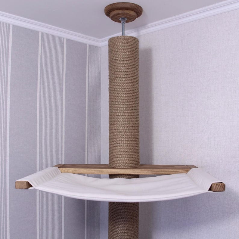 May include: A ceiling-mounted cat tree with a sisal-wrapped post and a wooden platform supporting a white hammock. The top features a wooden cap. The cat tree is designed to be installed in a corner.