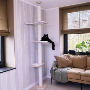 May include: A tall, off-white cat tree with multiple platforms and a scratching post. A sleek black cat is lounging on one of the platforms. The cat tree is in a room with a neutral color scheme and a window with natural light.