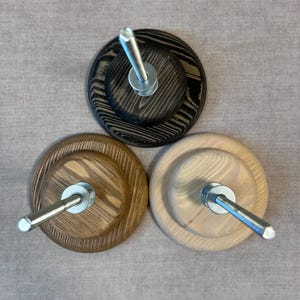May include: Three wooden bases with metal rods for displaying yarn or thread. The bases are stained in different shades of brown, black, and natural wood.