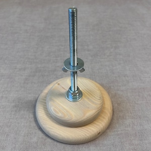 May include: A wooden base with a metal screw and wing nut. The base is made of two stacked wooden circles.