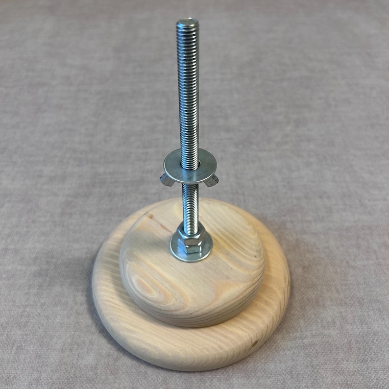 May include: A wooden base with a metal screw and wing nut. The base is made of two stacked wooden circles.