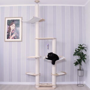Op de afbeelding: Een kattenboom met meerdere niveaus en een zwarte kat die op een hangmat ligt. De kattenboom heeft verschillende platforms, krabpalen en een hangend speeltje. De structuur is gemaakt van lichtgekleurd hout en beige stof, tegen een gestreepte muur.