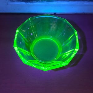 May include: A vibrant green glass bowl with a geometric, faceted design. The bowl has a circular base and a wide, open top. The glass has a vintage appearance, with a bright, almost neon, green colour.