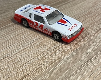 May include: White and red toy car with the number 24 and the word "Buick" on the side. The car has a blue stripe and the words "Carolina Kid" on the roof.