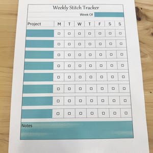 May include: A printable weekly stitch tracker with a teal blue background. The tracker has a section for project names and a grid for marking days of the week. There is also a section for notes.