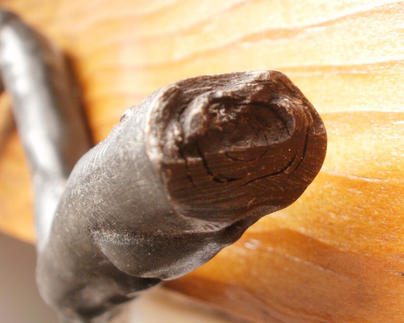 May include: Close-up of a dark brown wooden handle with a rough, textured surface. The handle is curved and has a slight bend.