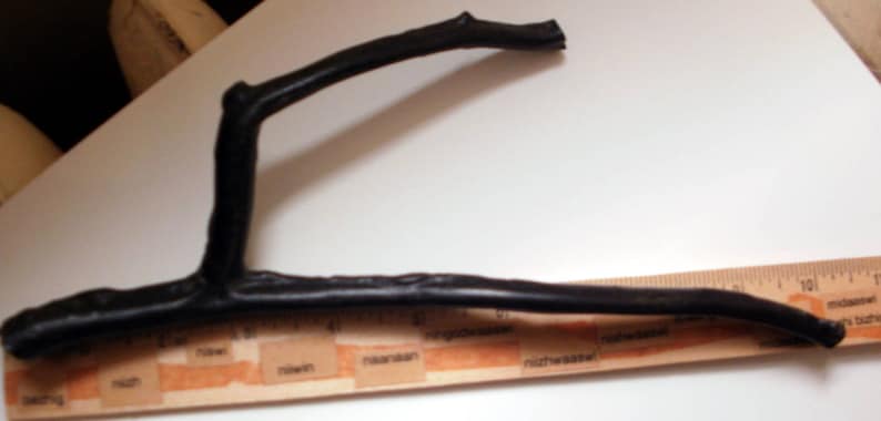 May include: A black, curved, wooden branch, approximately 12 inches long, is placed on top of a wooden ruler with markings in inches.