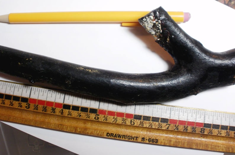 May include: A black wooden ruler with red and black markings. The ruler is labeled "DRAWRIGHT S-663". A black branch with a rough texture is placed on top of the ruler.