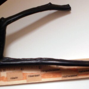 May include: A black, curved, wooden branch, approximately 12 inches long, is placed on top of a wooden ruler with markings in inches.