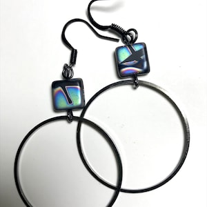 May include: A pair of black hoop earrings with iridescent square glass charms. The hoops are thick and have a smooth finish.