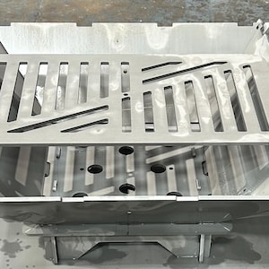 May include: A silver metal fire pit with a removable grate. The grate has a geometric pattern of cutouts.