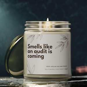 Pode incluir: Uma vela branca num frasco de vidro com tampa dourada. A vela tem um rótulo que diz "Smells like an audit is coming". O rótulo também diz "100% natural soy wax blend, Eco-friendly | non-toxic | vegan".