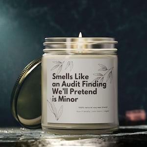 Può includere: Una candela bianca in un barattolo di vetro con un coperchio dorato. L'etichetta recita "Smells Like an Audit Finding We'll Pretend is Minor". 100% miscela di cera di soia naturale. Ecologica e non tossica, vegana.