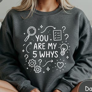 Peut inclure: Sweat-shirt gris chiné foncé avec l'inscription blanche "YOU ARE MY 5 WHYS" et des éléments graphiques. Le design comprend une loupe, une ampoule et des points d'interrogation. Vêtement décontracté.