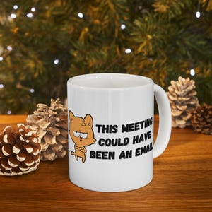 May include: White ceramic coffee mug with a cartoon cat and the text "This meeting could have been an email".