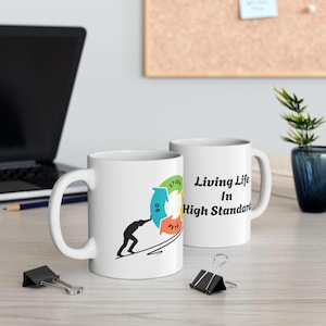 Peut inclure: Deux mugs en céramique blancs. L'un des mugs présente un motif circulaire coloré avec les mots "Study, Do, and My Life". L'autre mug porte l'inscription "Living Life In High Standard". Les deux mugs sont sur une surface claire.