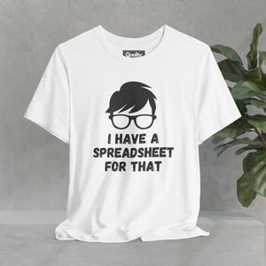 Pode incluir: Camiseta branca com um gráfico preto de uma pessoa usando óculos e o texto "Eu tenho uma planilha para isso".