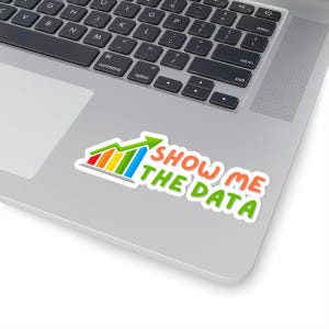 Puede incluir: Una pegatina con un gráfico de barras de colores y una flecha apuntando hacia arriba. El texto "SHOW ME THE DATA" está escrito en una fuente divertida.