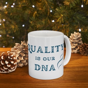 May include: White ceramic mug with a blue design that says "QUALITY IS OUR DNA" with a stylized DNA double helix graphic.