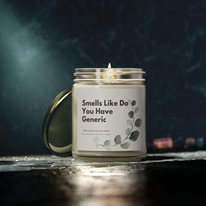May include: A lit candle in a clear glass jar with a silver lid. The label reads "Smells Like Do You Have Generic" with a eucalyptus design. The candle is on a dark surface with a blurred background.
