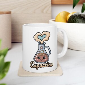 May include: White ceramic mug featuring a cartoon illustration of a beaker with a face, steam shaped like a heart, and the word "Capaccino". The beaker is filled with a brown liquid, and the design has a whimsical, coffee-themed aesthetic.