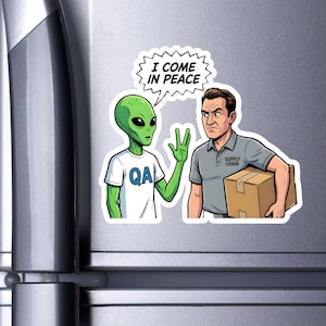 Op de afbeelding: Een sticker met een groene alien in een wit t-shirt met "QA", die vrede gebaart naar een man met een kartonnen doos. De alien zegt "I COME IN PEACE" in een tekstballon. De man draagt een grijs poloshirt met "SUPPLY CHAIN".