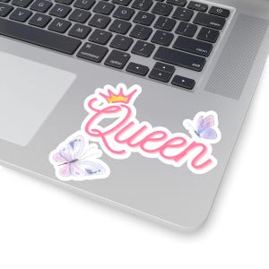 May include: Pink and white sticker with the word "Queen" in a pink cursive font with a gold crown above the word. Two purple butterflies are on either side of the word.