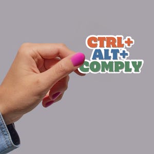 以下が含まれることがあります： 「CTRL+ALT+COMPLY」とカラフルな文字で書かれたステッカーを手に持っている。ステッカーは白地に黒のアウトラインで囲まれている。