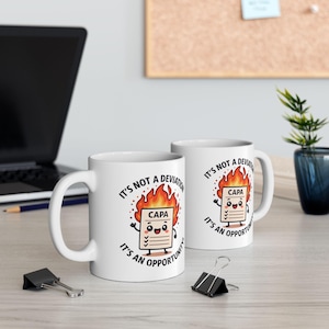 Puede incluir: Dos tazas de cerámica blanca con el texto "IT'S NOT A DEVIATION, IT'S AN OPPORTUNITY!" y un documento de dibujos animados en llamas. El documento dice "CAPA". Las tazas están sobre una superficie clara.