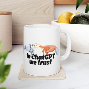 Puede incluir: Taza de cerámica blanca con un gráfico de una mano robótica y una mano humana tocándose, con el texto "In ChatGPT we trust".