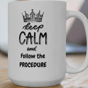 Könnte beinhalten: Weiße Keramik-Tasse mit schwarzer Krone und dem Text "Keep Calm and Follow the Procedure". Die Tasse mit Henkel ist für Heißgetränke wie Kaffee oder Tee geeignet.