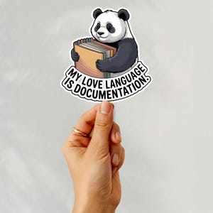 Könnte beinhalten: Ein Aufkleber mit einem schwarz-weißen Panda, der Bücher hält. Der Aufkleber hat den Text "MY LOVE LANGUAGE IS DOCUMENTATION" in einem geschwungenen Banner. Der Aufkleber wird von einer Hand gehalten.