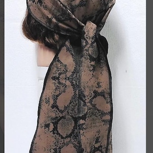 May include: A head wrap featuring a tan and black snakeskin print pattern. The fabric is tied at the back with two long, hanging tails. The edges are finished with a black stitched hem, and the material covers the top and sides of the head.