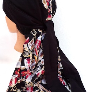 May include: A black head wrap with a musical instrument pattern. The wrap features a black base with a design of guitars, drums, and other instruments in red, white, and gold. The wrap is tied at the back.