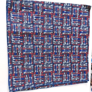 May include: Square fabric with a repeating pattern of white and red arrows on a dark blue background. The arrows are arranged in a grid-like design, creating a geometric and symmetrical appearance. The fabric has a textured look.