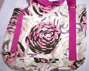 May include: A large tote bag with a floral pattern featuring pink, brown, and gray roses on a cream background. The bag has bright pink handles and straps.