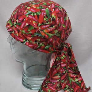 May include: A red and green chili pepper patterned bandana. The bandana is tied at the back and has long ties. The fabric is covered in a repeating pattern of red and green chili peppers.