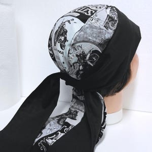 May include: A black and white bandana with a motorcycle and biker theme. The bandana features a patchwork design with various motorcycle-related graphics and text. The bandana is tied at the back, with long ties hanging down.