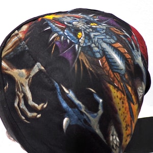 May include: Black head wrap featuring a detailed dragon design. The dragon is depicted in shades of blue, orange, and yellow, with sharp claws and a fierce expression. The head wrap is made of a soft, dark fabric.