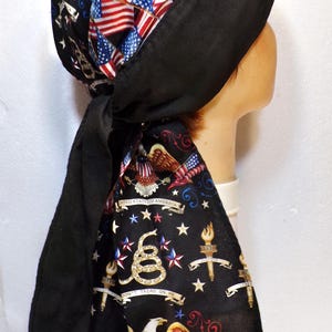 May include: A black head wrap featuring a patriotic design. The wrap's top section is covered in American flags, while the ties display an eagle, stars, and the phrase "Don't Tread on Me."