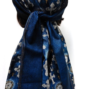 May include: A blue denim head wrap featuring a pattern of ornate crosses and sunburst designs. The head wrap is tied at the back, with long, flowing ties. The fabric has a textured appearance.