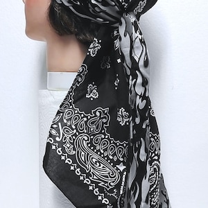May include: Black bandana head covering with a paisley and flame design. The head covering is tied at the back and is displayed on a mannequin head. The bandana features a black background with white paisley patterns and gray flame accents.