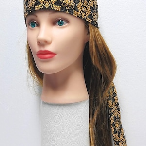 May include: A black and gold Harley-Davidson headwrap with a repeating floral pattern. The headwrap features the Harley-Davidson logo in silver and orange with rhinestones. The headwrap is on a mannequin head.