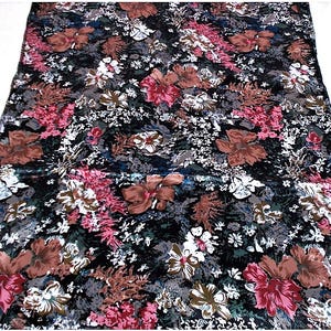 May include: A floral fabric with a dark background, featuring large brown, pink, and white flowers. The pattern includes smaller white blossoms and gray foliage, creating a dense, textured design. The fabric is likely used for clothing or home decor.