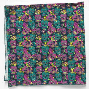 May include: A square, dark navy fabric with a repeating pattern of colorful sugar skulls and roses. The skulls are teal, pink, and yellow, with intricate details. The roses are pink and yellow, and the overall design is vibrant and eye-catching.
