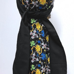 May include: A black head wrap with a patterned design. The pattern includes yellow, blue, and green shapes on a black background. The wrap has long, solid black ties.